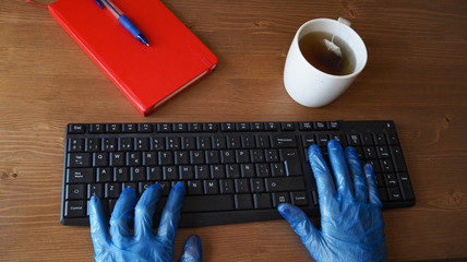 Gloved hands to protect themselves from the coronavirus by typing a computer in an office. Coronavirus security measures