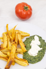 French fries and spinach on the plate with tomato in the background