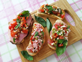 Homemade Italian bruschetta with cherry tomatoes, ham, Basil leaves, cheese and pesto sauce on a...