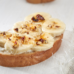 Sandwich with banana slices sprinkled with nuts close up on a white wooden table.
