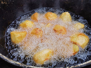 Whole potatoes are fried in a deep black cauldron with a lot of oil . Unhealthy lifestyle diet, fat and greasy fast food