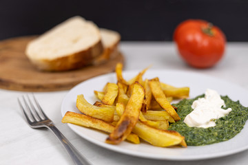 Fried potatoes with spinach on the plate with sliced bread in the background