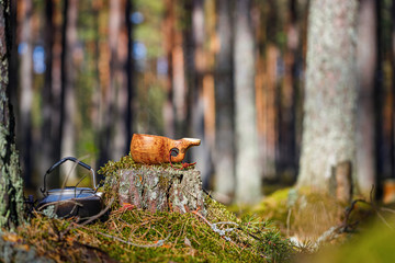 A wooden mug kuksa with a teapot stand on a stump in the forest. Blurred background.
