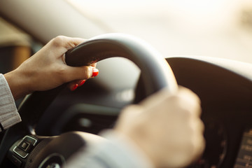 Closeup of woman's hands on a steering wheel driving safe isolated during coronavirus pandemic quarantine. Girl's hands with red nails holding a wheel and drive a car. Private transport concept.