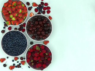 Strawberries, raspberries, 
cherry and blueberries on a turquoise background, background concept and creative layout. Flat lay. Top view.