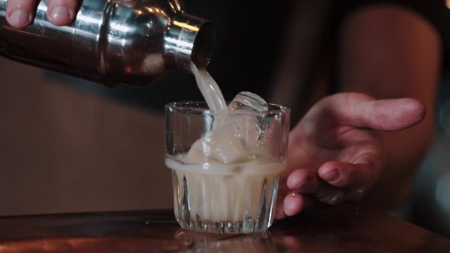 The bartender pours white coctail into a glass with ice.Close-up