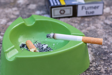 Cendrier vert avec une cigarette et un paquet de cigarettes