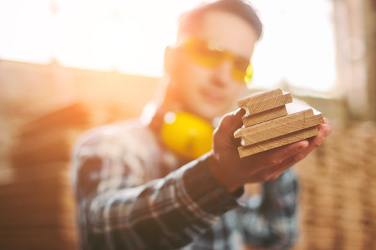 Professional male carpenter in protective eyewear and headphones working with wooden material at sawmill factory. Young skilled cabinet maker at woodworking workshop. Lumber furniture production mill