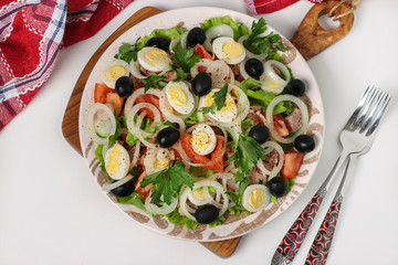 Healthy salad with canned tuna, tomatoes, quail eggs, black olives, white onions and organic lettuce on white background, Top view, Closeup