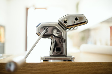 Kitchenware: pasta machine on a wooden table, ready to make fresh home-made pasta, side view.