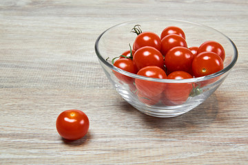 still life - cherry tomatoes in a glass bowl and another one near, on a wooden table surface