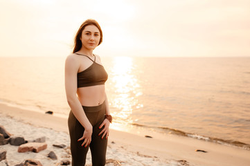 Fototapeta na wymiar Portrait of a young beautiful athletic girl in sportswear on the seashore at sunset