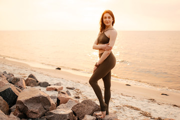 Fototapeta na wymiar Attractive young athletic girl in sportswear on the seashore at sunset