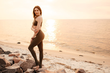 Attractive young athletic girl in sportswear on the seashore at sunset