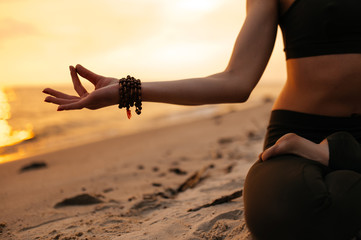 Meditating girl on the seashore during sunset. She is sitting in a lotus position. Close-up photo