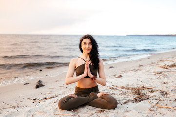 Fototapeta na wymiar A young girl sits in a lotus position on the seashore at sunset. Girl practices yoga by the sea