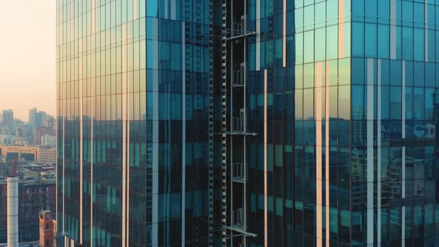 Aerial elevator shot of glassed skyscraper exterior with a reflection of the cityscape in the windows