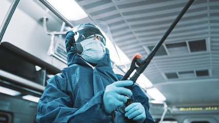 Portrait of an african worker with protective suit, face shield and medical mask disinfecting train.