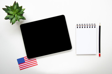 Tablet mockup with black screen and USA flag on a white desktop. Flat lay Learn a language at home...