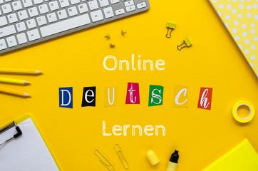 ONLINE DEUTSCH LERNEN sign on a student table framed withoffice stationery and pc keyboard. Top view on a yellow background - obrazy, fototapety, plakaty