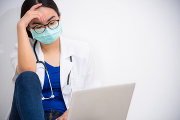 Asian young woman doctor wear mask to safety Coronavirus sit on the floor looking at the laptop with sadness, stress and worry about the problem, Concept take care yourself stop the epidemic Covid-19