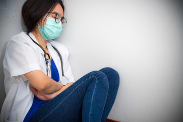 Asian young woman doctor wear mask to safety Coronavirus sit on the corner floor sleeping with exhaustion from overwork concept take care yourself is to help physician stop the epidemic Covid-19 virus