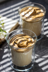 Dalgona Coffee in transparent glasses on a windowsill illuminated by sunlight.