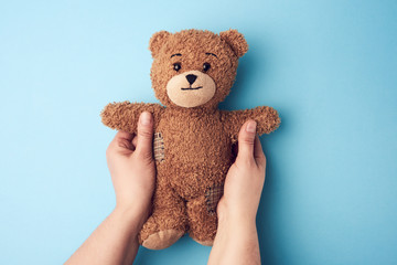 two female hands hold a small brown toy teddy bear on a blue background