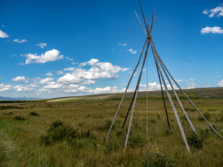 Nez Perce teepee frames with white billowing clouds and blue sky in background. © Kathryn