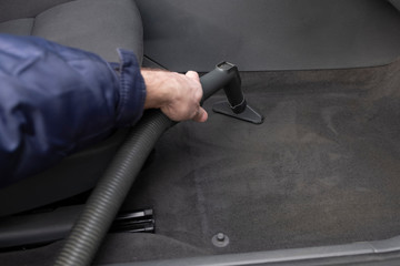Hand of a man. A man vacuums a car interior.