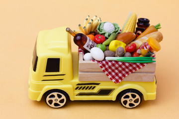A yellow toy truck delivering food and drinks in a wooden box. Food supply  and food donation concept.