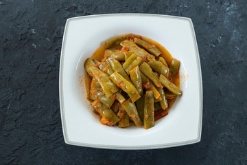 Green beans with olive oil in the white plate on the black background.