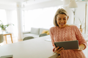 Close photo of blonde woman with beautiful smile wearing pink sweater while using tablet computer...