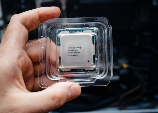 Paris, France - May 31, 2019: Close-up of engineer male hand holding new professional Intel Xeon E5-2687w v4 CPU processor in plastic blister unboxing with Dell Precision Workstation in the background