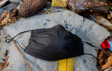 One black protective face mask to prevent fast spreading coronavirus originated in Wuhan, China. Concept of a couching mask laying on top of a rubbish outdoor ground/background. In Medellin, Colombia.