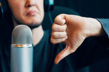 Streamer online gamer with headphones and a microphone at the computer shows dislike gesture. Man...