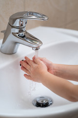 Little girl is washing her hands under water in the white bathroom