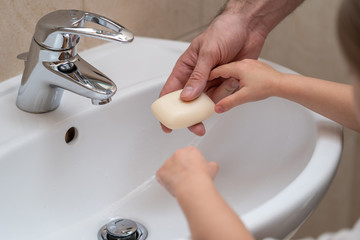 Father is washing hands of his baby toddler, rubbing with soap for corona virus prevention, hygiene to stop spreading coronavirus. Concept of teaching and learning healthy habits from an early age.