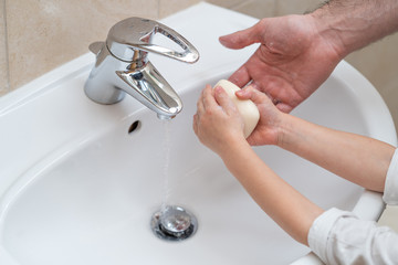 Father is washing hands of his baby toddler, rubbing with soap for corona virus prevention, hygiene to stop spreading coronavirus. Concept of teaching and learning healthy habits from an early age.
