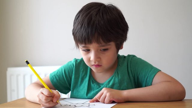 Portrait school kid siting on table doing homework, Happy Child boy holding pencil writing, A boy drawing on white paper at the table, Elementary school and home schooling, Distance Education concept 