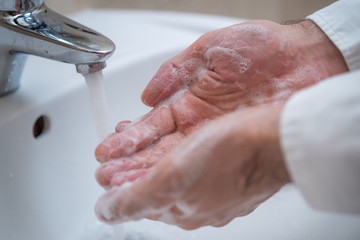Fototapeta premium Close-up of man washing hands with soap under bathroom sink.