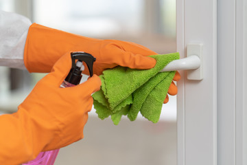 man disinfects door in orange gloves with disinfectant liquid. spraying door handle and wiping with a cloth. Disinfection of premises.prevention coronavirus, infectious diseases. window washing.