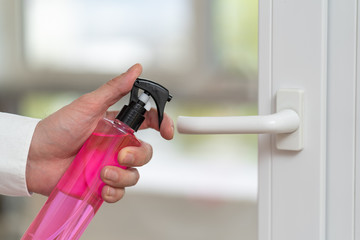 Close up view of men hand using pink sanitizer for disinfecting home door link.