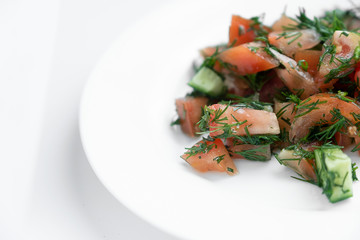 Tomato and cucumber salad sprinkled with herbs, on a white plate.
