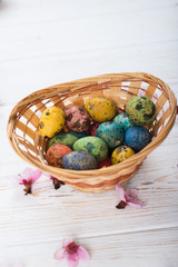 Multi-colored Easter eggs in a basket on a white wooden background