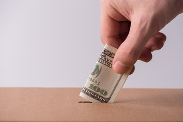 Donation payment pay big money concept. Cropped close up photo of male hand putting one hundred american banknote into the cardboard box
