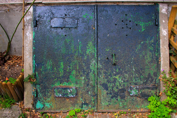 Double door in worn and rusty metal, painted green. Access to an underground cellar.