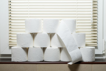 Piles of rolls of toilet paper stand on the windowsill in the toilet