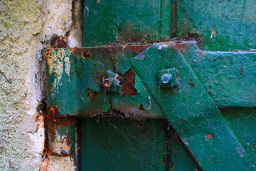 Rusty metal hinge on a worn wooden door painted green.