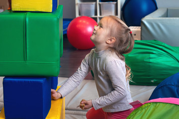 girl in playroom plays with soft cubes and builds a pyramid